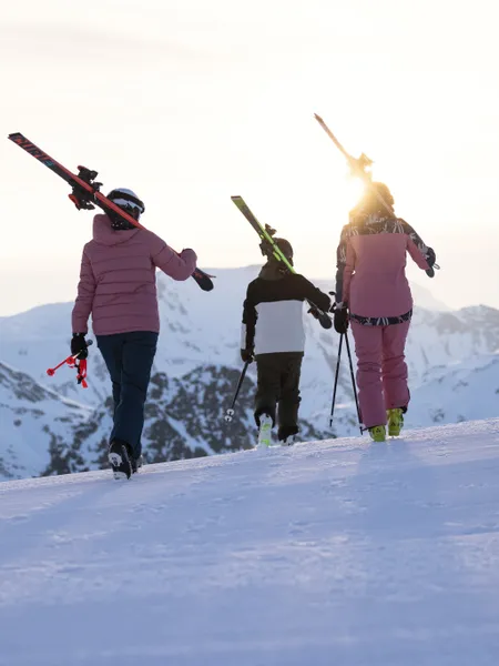 Skiers carrying skis at sunset on snowy mountain ridge