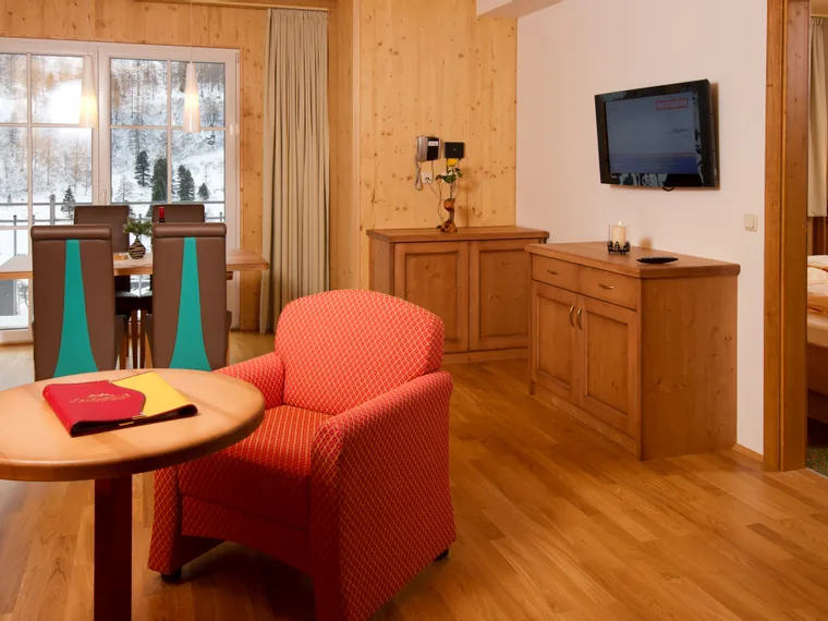 Cozy alpine hotel suite with wooden furniture, red armchair, and snow-covered mountain view