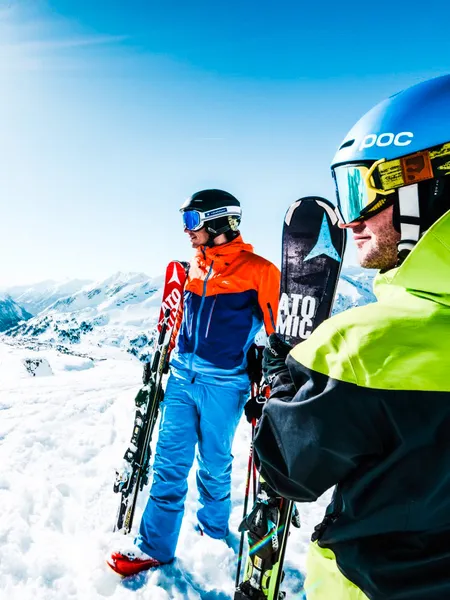 Two skiers with gear overlooking sunny Alpine mountain landscape