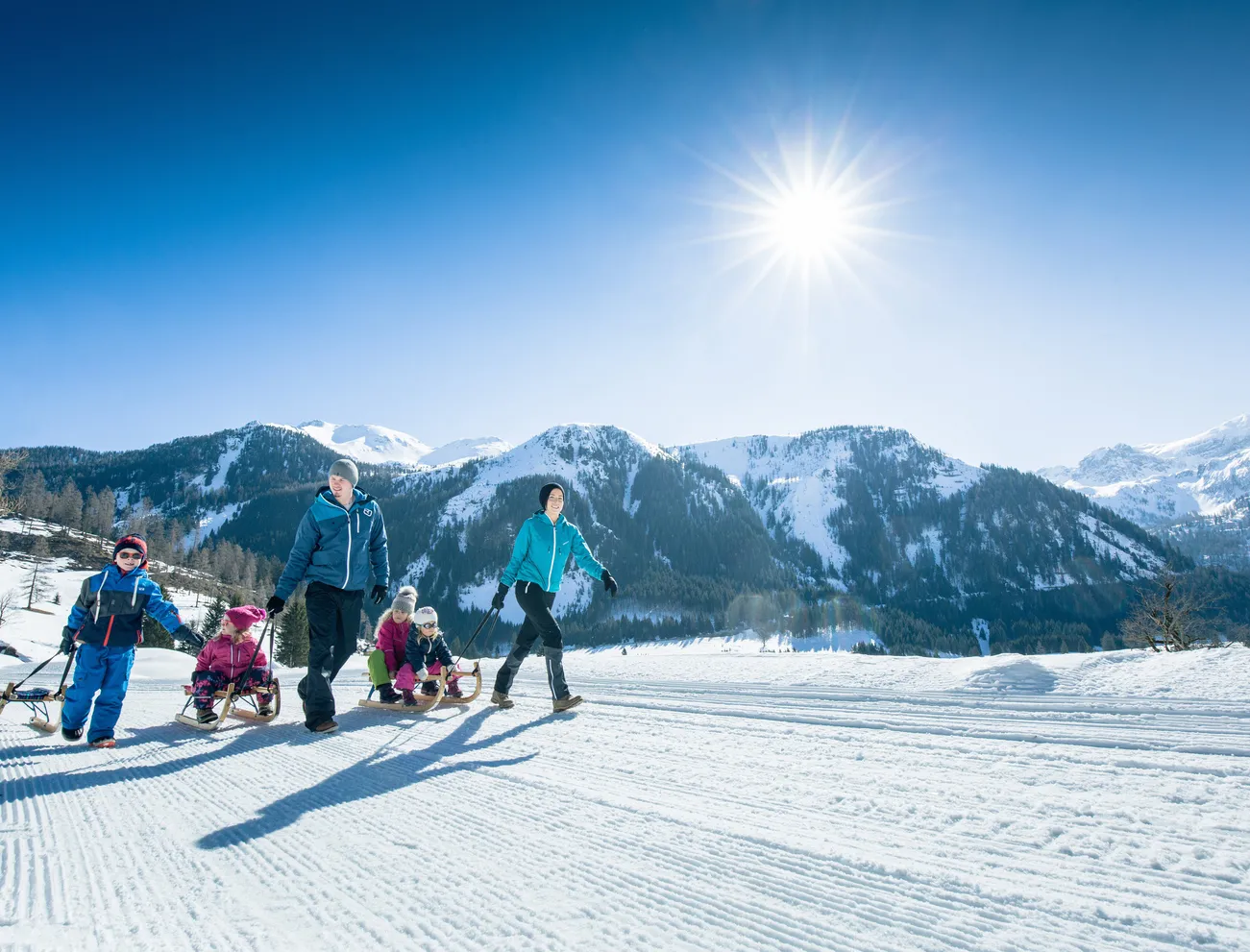 Family pulling sleds on a sunny winter vacation in the snowy Alps