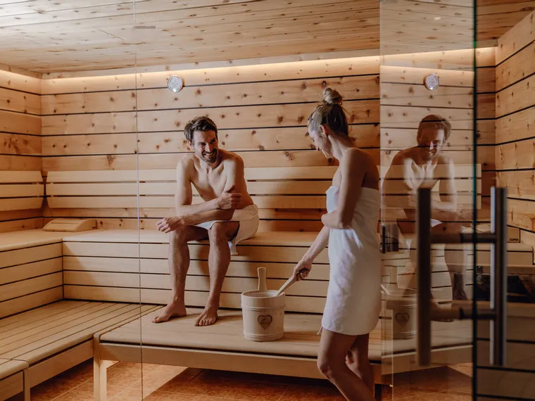Paar entspannt in einer Holzsauna mit Eimer und Schöpfkelle