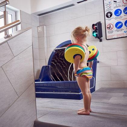 Small child with floatation armbands stands near indoor pool slide