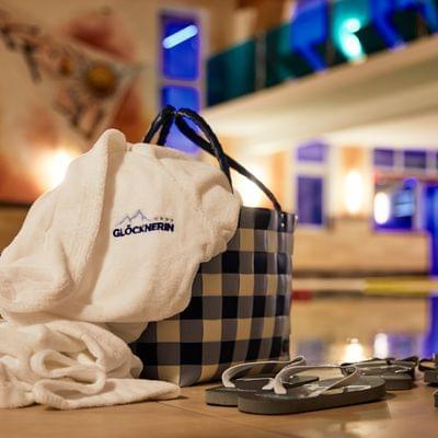 Wellness-Bademantel mit Glocknerin-Logo neben Korb und Flip-Flops am Innenpool