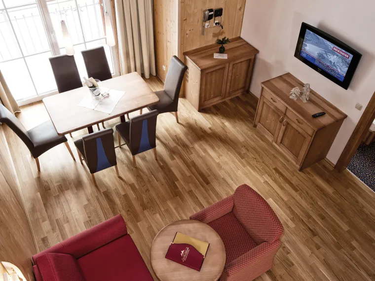 Cozy hotel room with wooden furniture, dining table, armchairs, and wall-mounted TV
