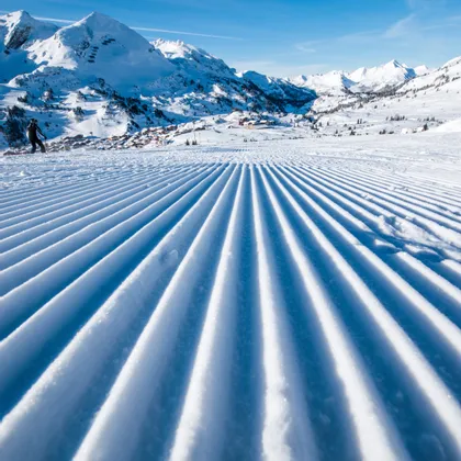 Groomed ski slope with alpine mountain view under clear blue sky