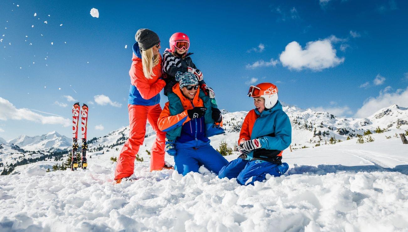 Familie spielt fröhlich im Schnee beim Skiurlaub in den Alpen
