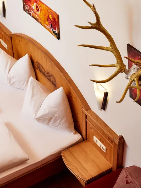 Cozy hotel room with double bed, wooden headboard, antler decor and modern wall lighting