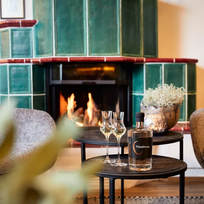 Hazelnut liqueur and glasses on table in front of green tiled fireplace