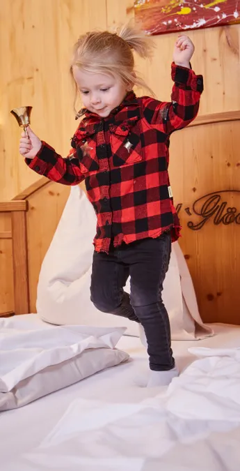 Happy little girl jumping on a hotel bed with wooden wall background