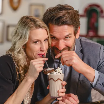 Couple sharing a chocolate milkshake with straws in a cozy café setting
