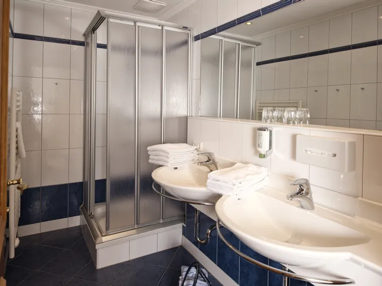 Modern hotel bathroom with double sink, glass shower, white towels and tiled walls