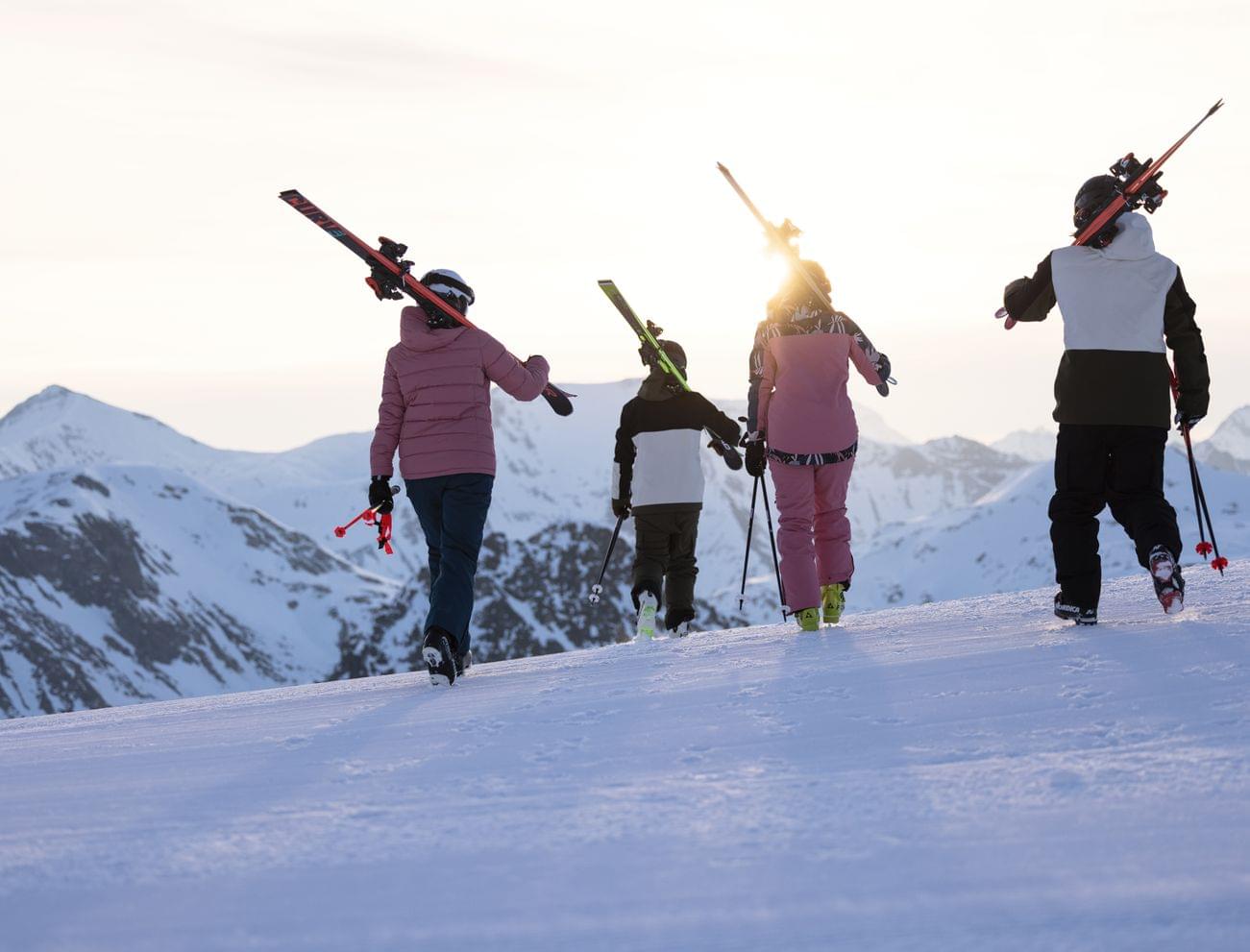 Skiers carrying skis at sunset on snowy mountain ridge