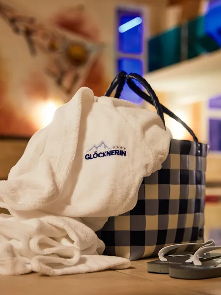 Spa robe with Glocknerin logo beside basket and flip-flops near indoor pool