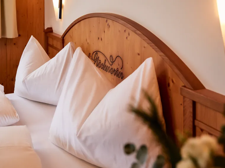 Gemütliches Hotelbett mit weißen Kissen und hölzernem Kopfteil mit Schriftzug Glocknerin