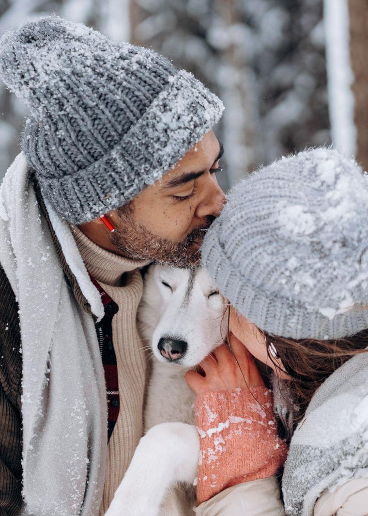 Paar in Winterkleidung kuschelt mit Husky im verschneiten Wald