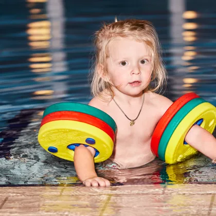 Young child with colorful swim aids in indoor pool near pool edge