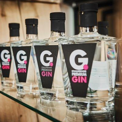 Reihe von G. Premium Gin Flaschen mit schwarzem Etikett auf einem Glasregal