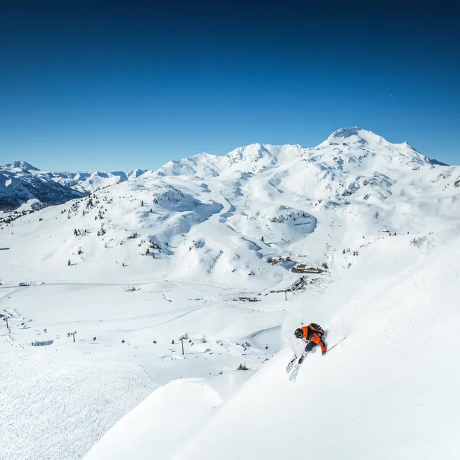 Skier in orange jacket carving through fresh powder on a steep alpine slope