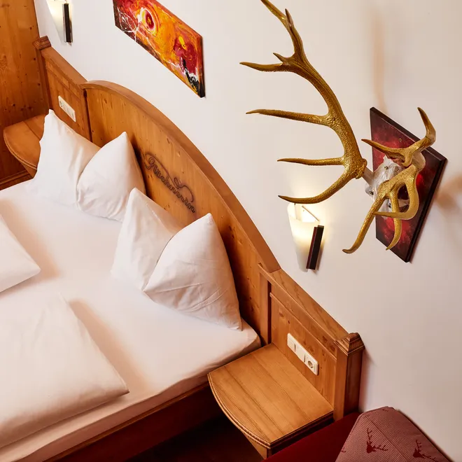 Gemütliches Hotelzimmer mit Doppelbett, Holz-Kopfteil, Geweihdeko und moderner Wandbeleuchtung