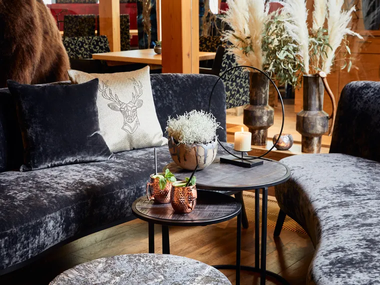 Cozy lounge area with velvet sofas, decorative pillows, candles, and Moscow mule cocktails