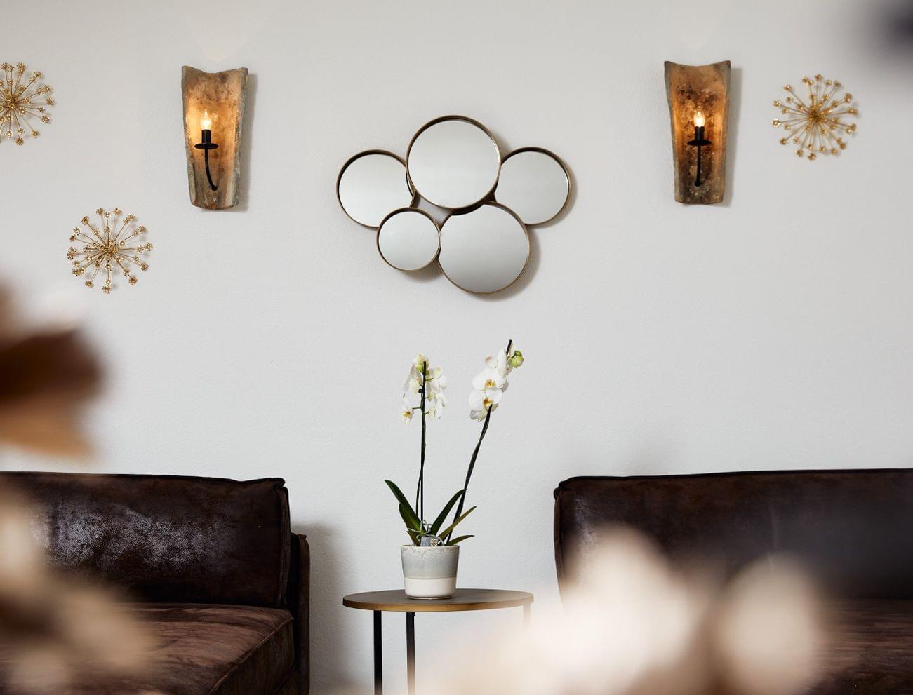 Modern living room with brown sofas, orchid plant, round wall mirrors and gold wall decor
