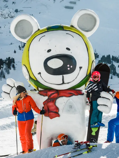 Family posing by giant bear mascot statue at snowy ski resort