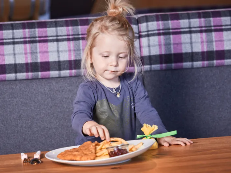Child eating french fries with schnitzel and ketchup at restaurant table