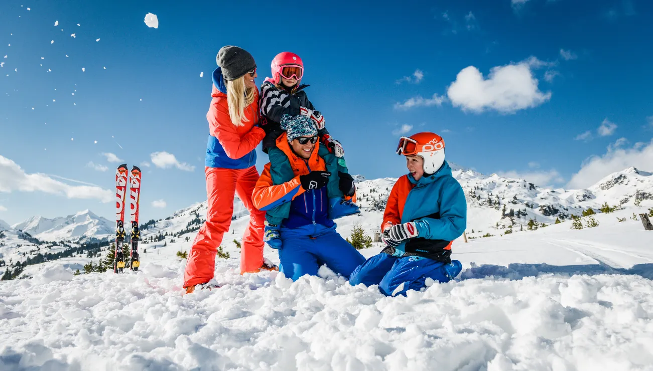 Familie spielt fröhlich im Schnee beim Skiurlaub in den Alpen
