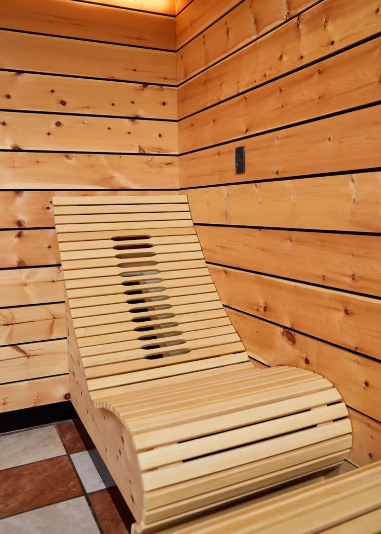 Ergonomic wooden lounger in a modern sauna with wood panel walls