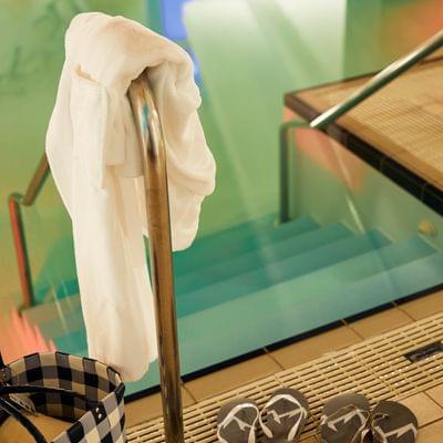 Badelatschen, Bademantel und Tasche neben einem Hallenpool mit Treppe