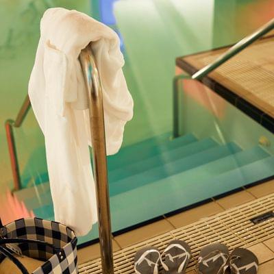 Flip-flops, bathrobe and bag beside indoor pool with stairs
