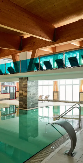 Modernes Hallenbad mit Holzdecke, Liegestühlen und Wasserfall-Dusche