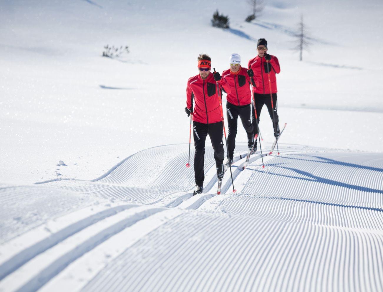 Three cross-country skiers in red jackets gliding on groomed snow trail