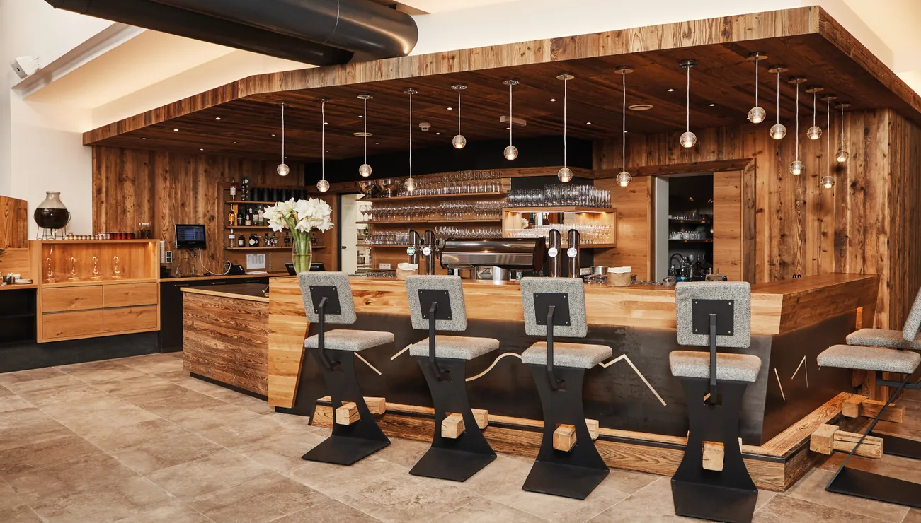 Moderne Bar im rustikalen Stil mit Holzverkleidung, Hängelampen und gepolsterten Barhockern