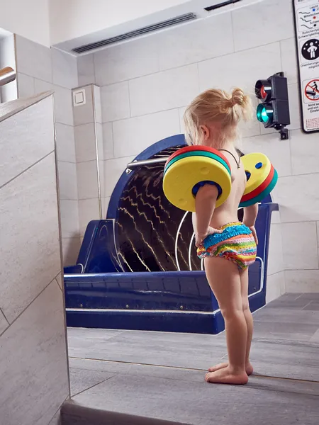 Small child with floatation armbands stands near indoor pool slide