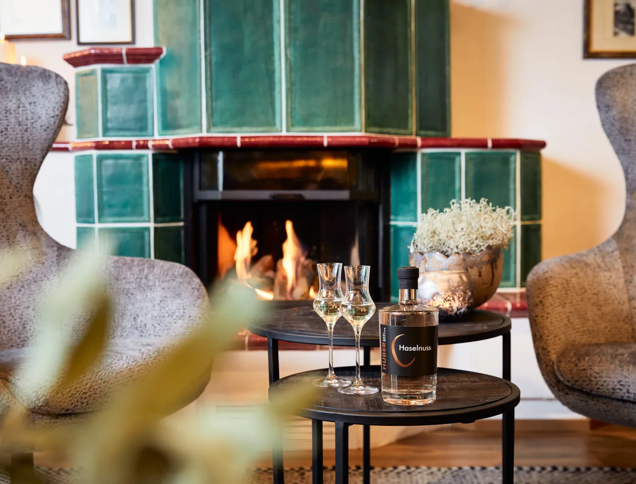 Hazelnut liqueur and glasses on table in front of green tiled fireplace