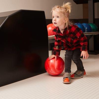 Kleines Mädchen mit rotem Bowlingball in einer Bowlingbahn