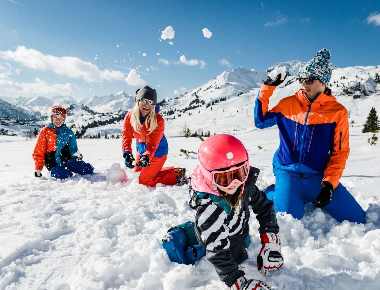Familie spielt im Schnee während Skiurlaub in sonnigen Alpenbergen