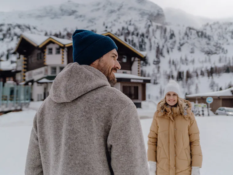 Paar in Winterkleidung vor schneebedeckten Chalets in den Alpen