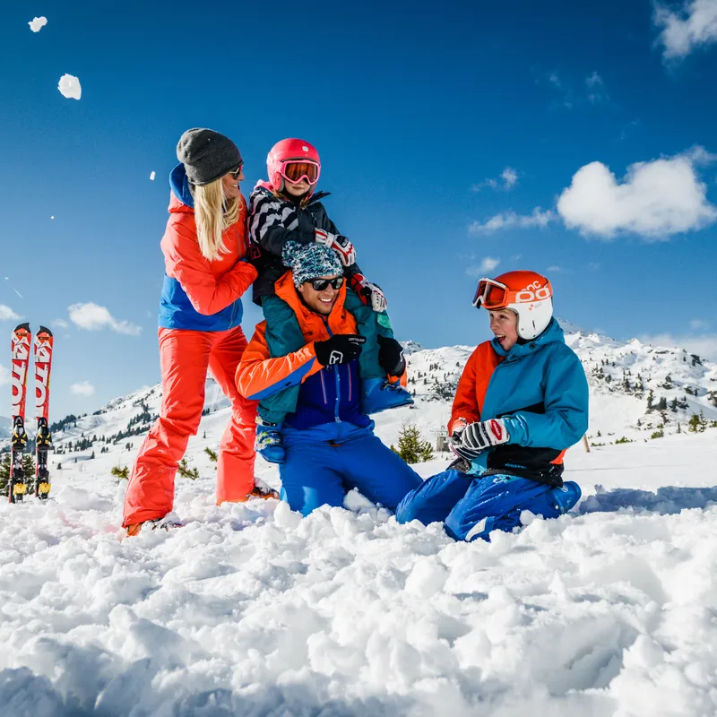 Familie spielt fröhlich im Schnee beim Skiurlaub in den Alpen
