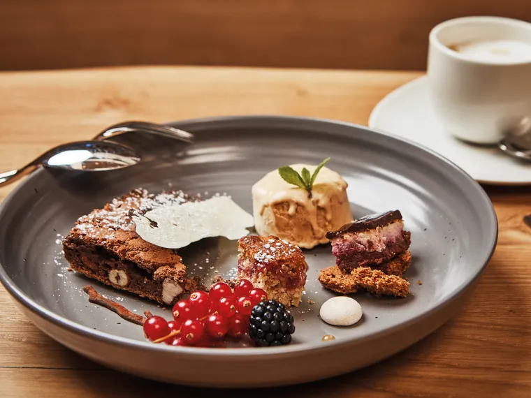 Gourmet dessert plate with brownie, ice cream, berry tart, red currants and espresso on wooden table