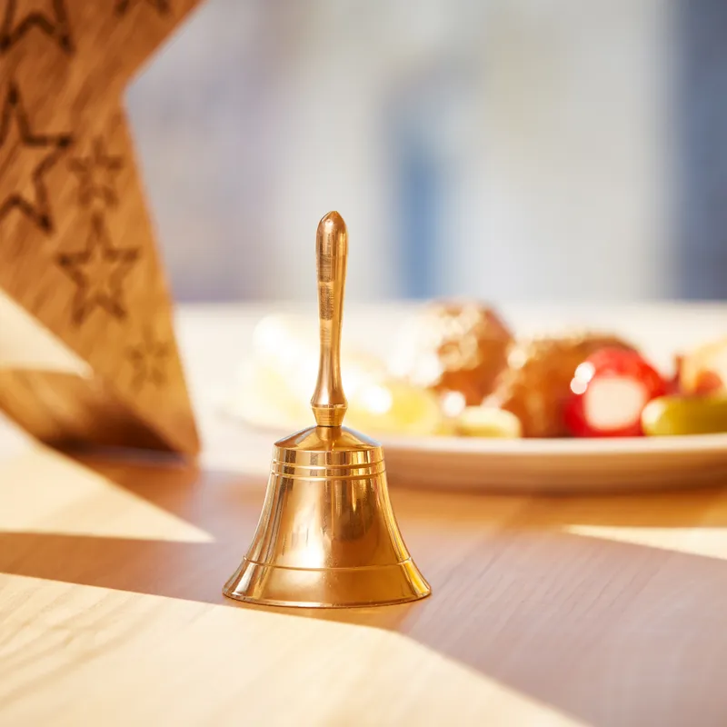 Golden hand bell on a wooden table with festive breakfast and juice