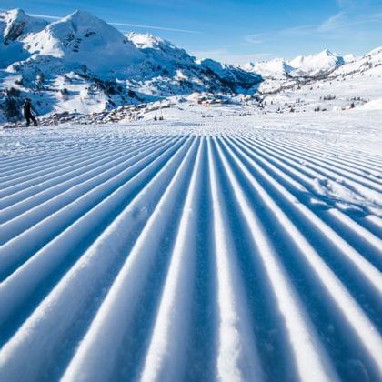 Groomed ski slope with alpine mountain view under clear blue sky