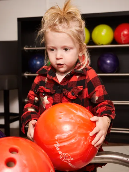 Young girl holding orange bowling ball at bowling alley