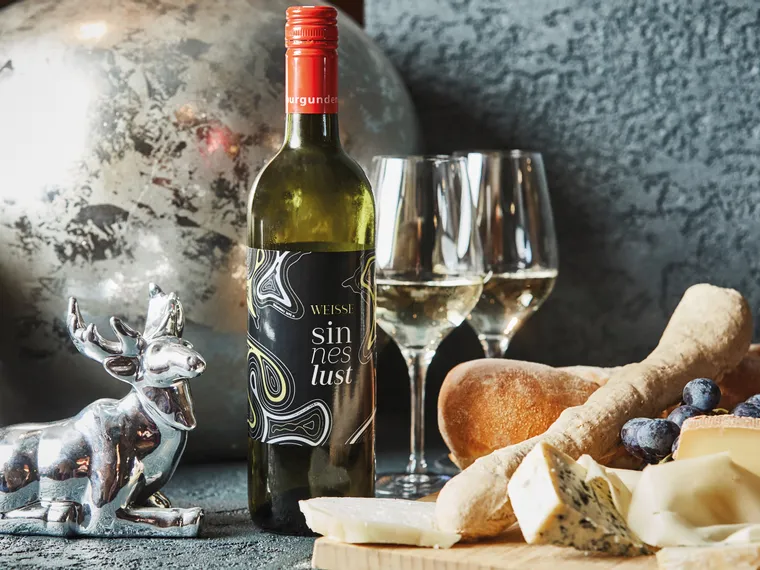 Flasche Weißwein mit Käse, Brot und Trauben auf einem gedeckten Tisch