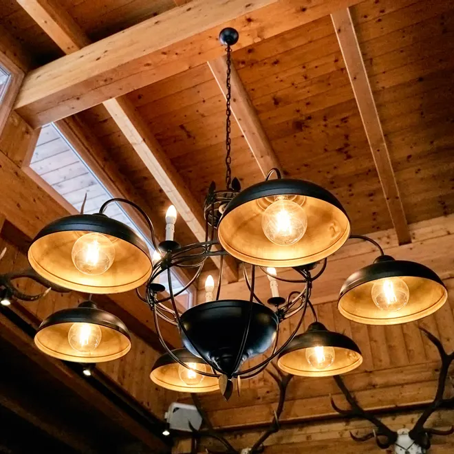 Rustic chandelier with exposed bulbs hanging from wooden ceiling with antlers