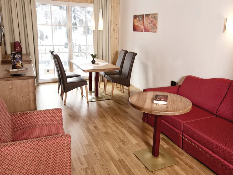 Gemütlicher Hotelwohnraum mit rotem Sofa, Esstisch und Bergblick durch Glastüren