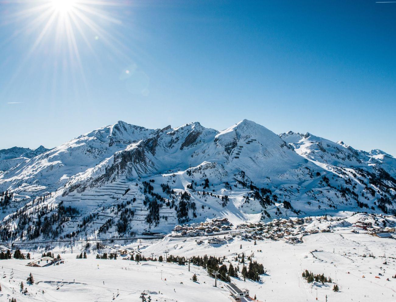 Verschneite Alpenlandschaft mit Skigebiet unter sonnigem, klarem Himmel