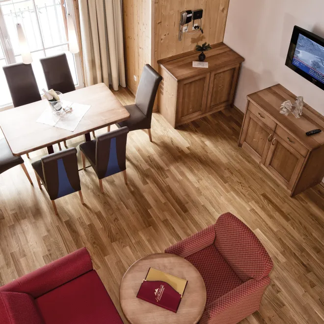 Cozy hotel room with wooden furniture, dining table, armchairs, and wall-mounted TV