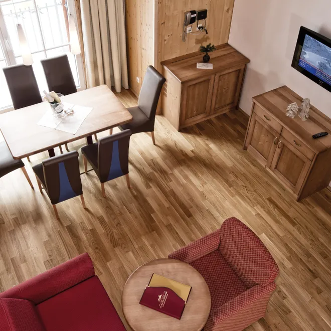 Gemütliches Hotelzimmer mit Holzmöbeln, Esstisch, Sesseln und wandmontiertem Fernseher